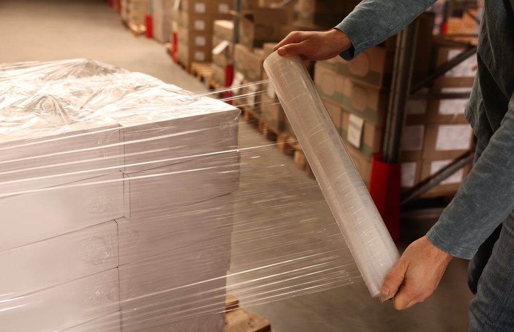 Worker,wrapping,boxes,in,stretch,film,at,warehouse,,closeup